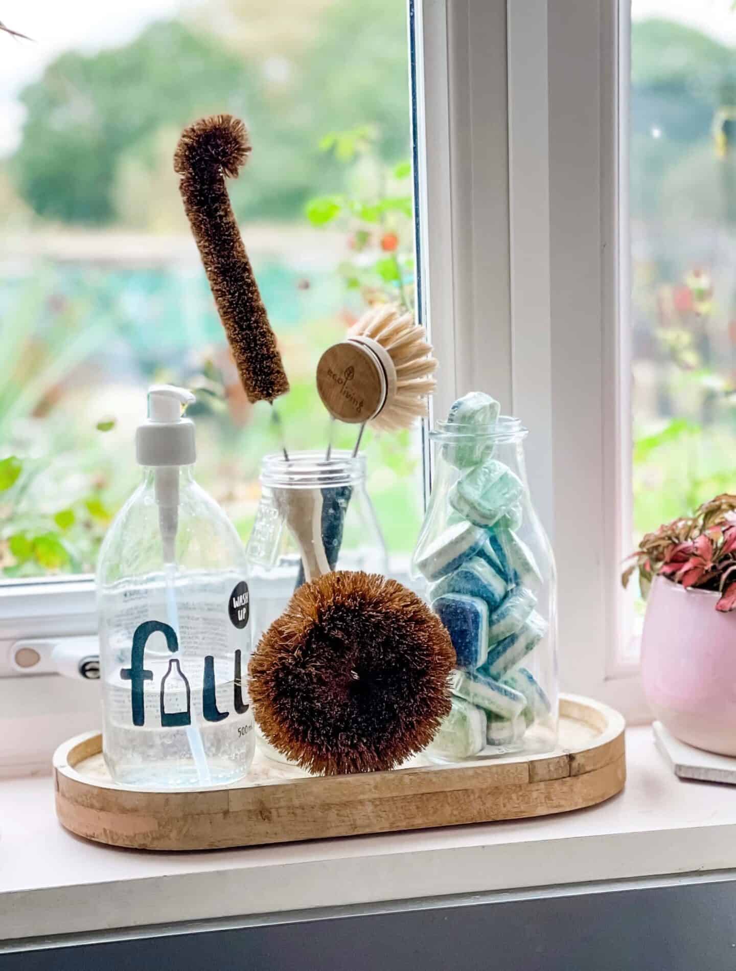 EcoZone dishwasher tables in a glass bottle on a windowsill with plastic-free washing up utensils and a glass refill bottle of washing up liquid help cut out chemicals and single use plastic in the home