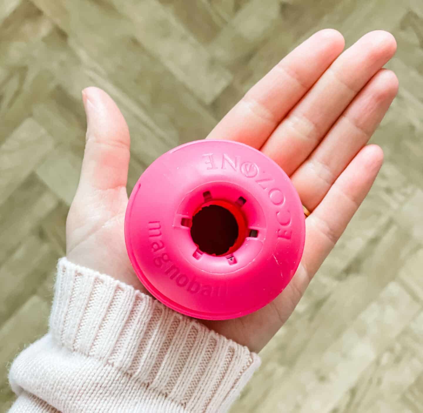 Hand holding a pink EcoZone Magnoball over a herringbone floor