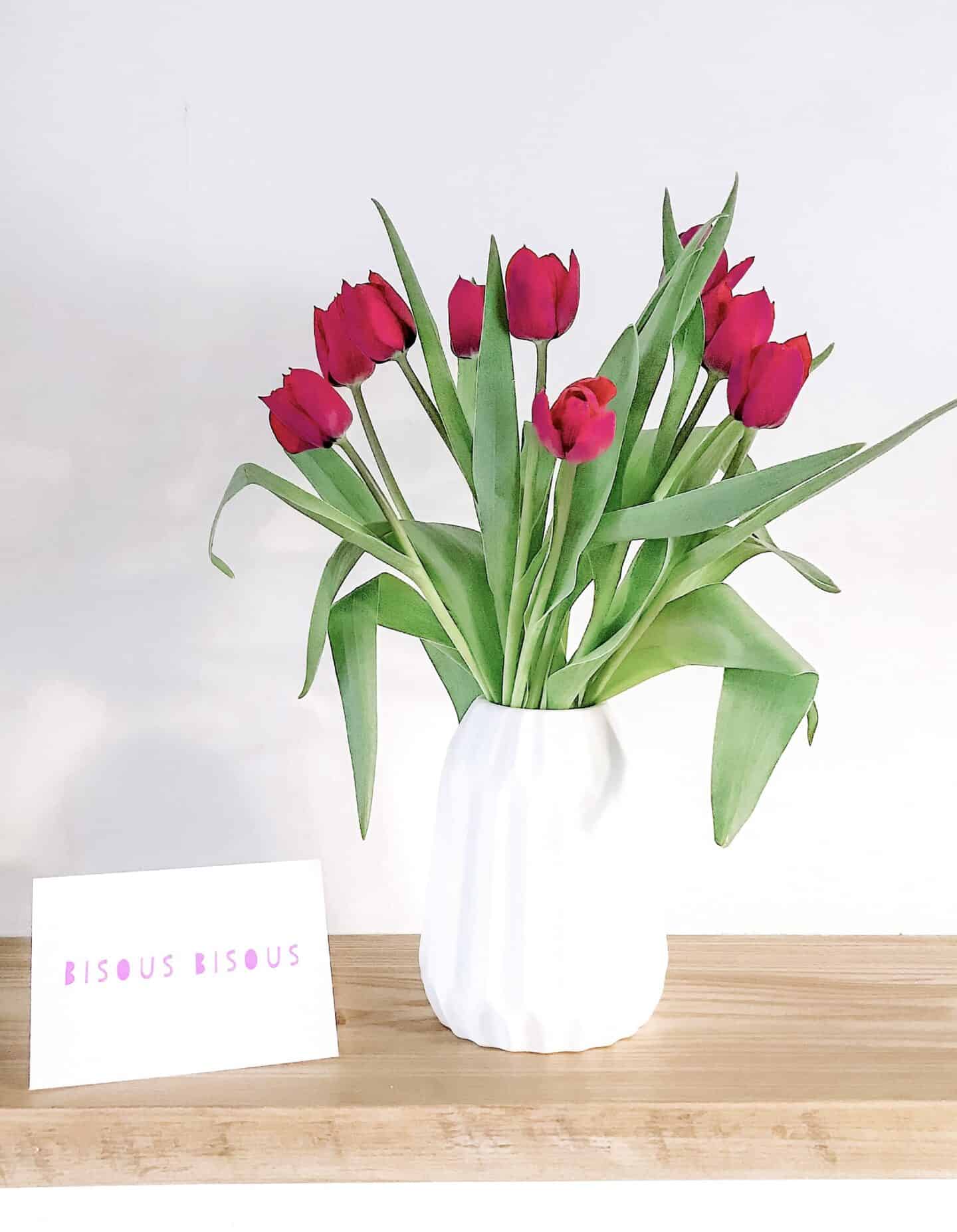Dark pink tulips in a white vase on an oak shelf