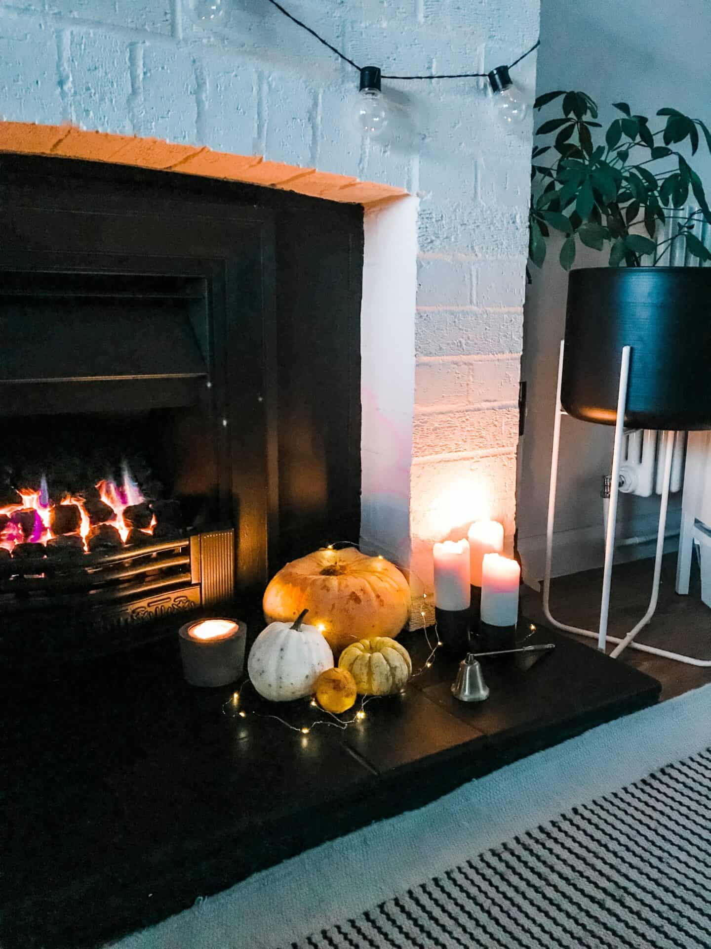 A black fireplace with sustainable Halloween decorations of real pumpkins, candles and fairylights